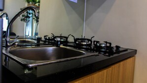 A kitchen with a stainless steel sink, a black countertop, and a stove. - Warm and Cozy 3BR Apartment at M-Town Residence (Gading Serpong)