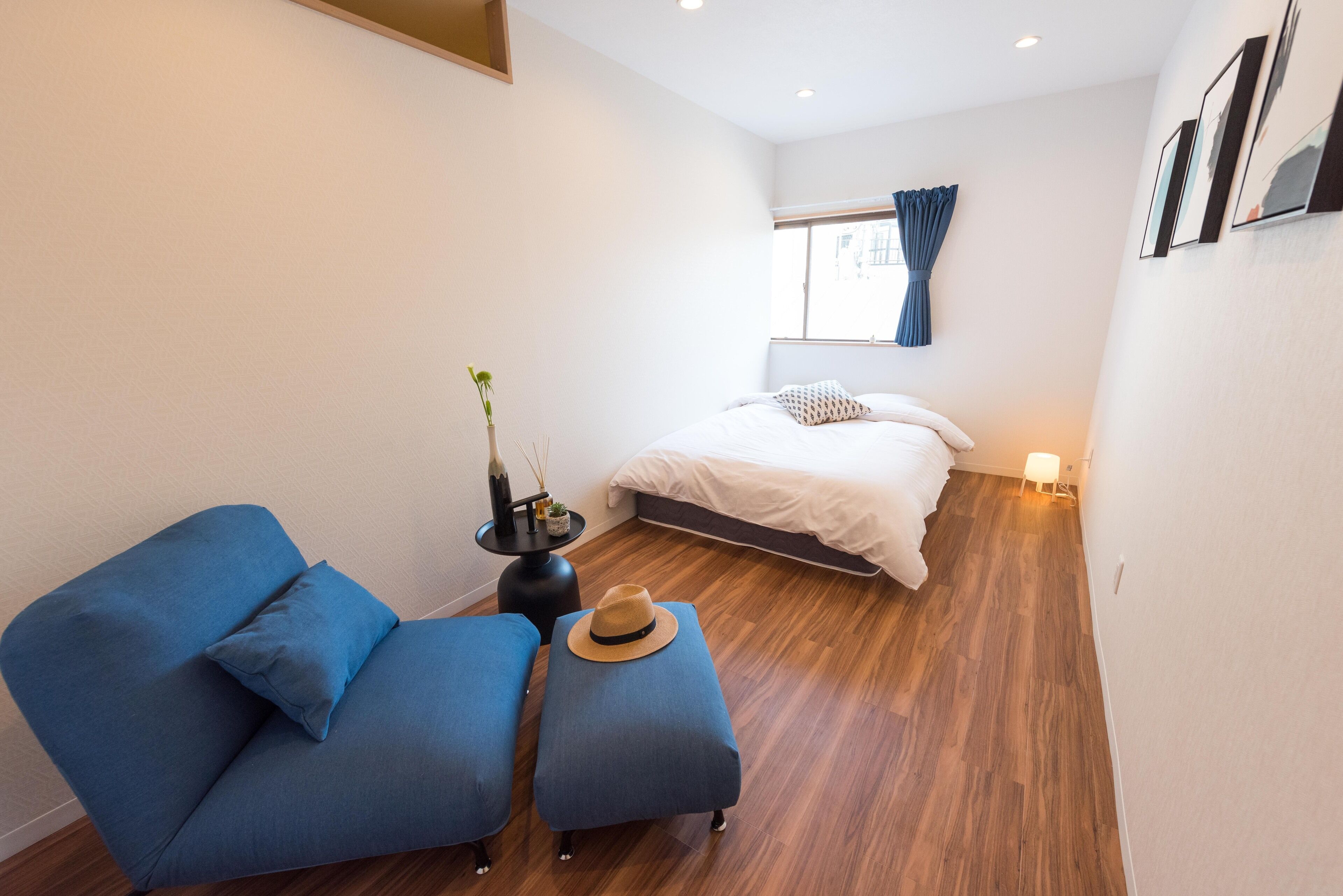 A compact room with a bed, a blue sofa, and a small table with a hat and a plant.