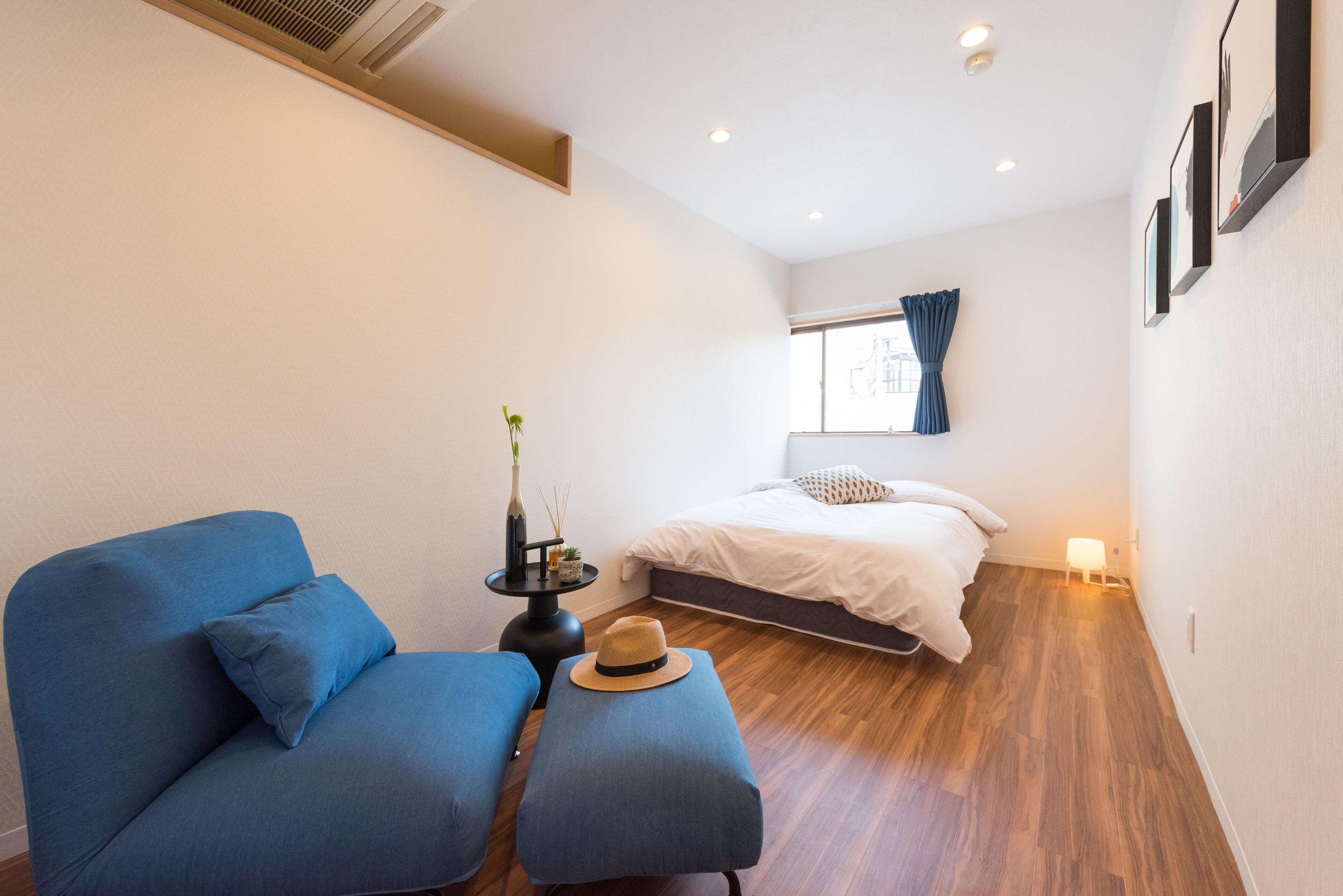 Een kleine kamer met een bed, een blauwe bank en een tafeltje met een hoed en een fles.