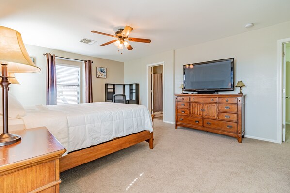 A bedroom with a bed, a dresser, a television, and a ceiling fan.