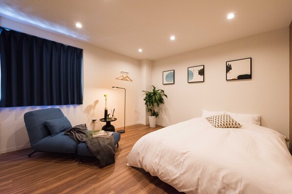 A modern bedroom with a large bed, a blue armchair, a floor lamp, and wall art.