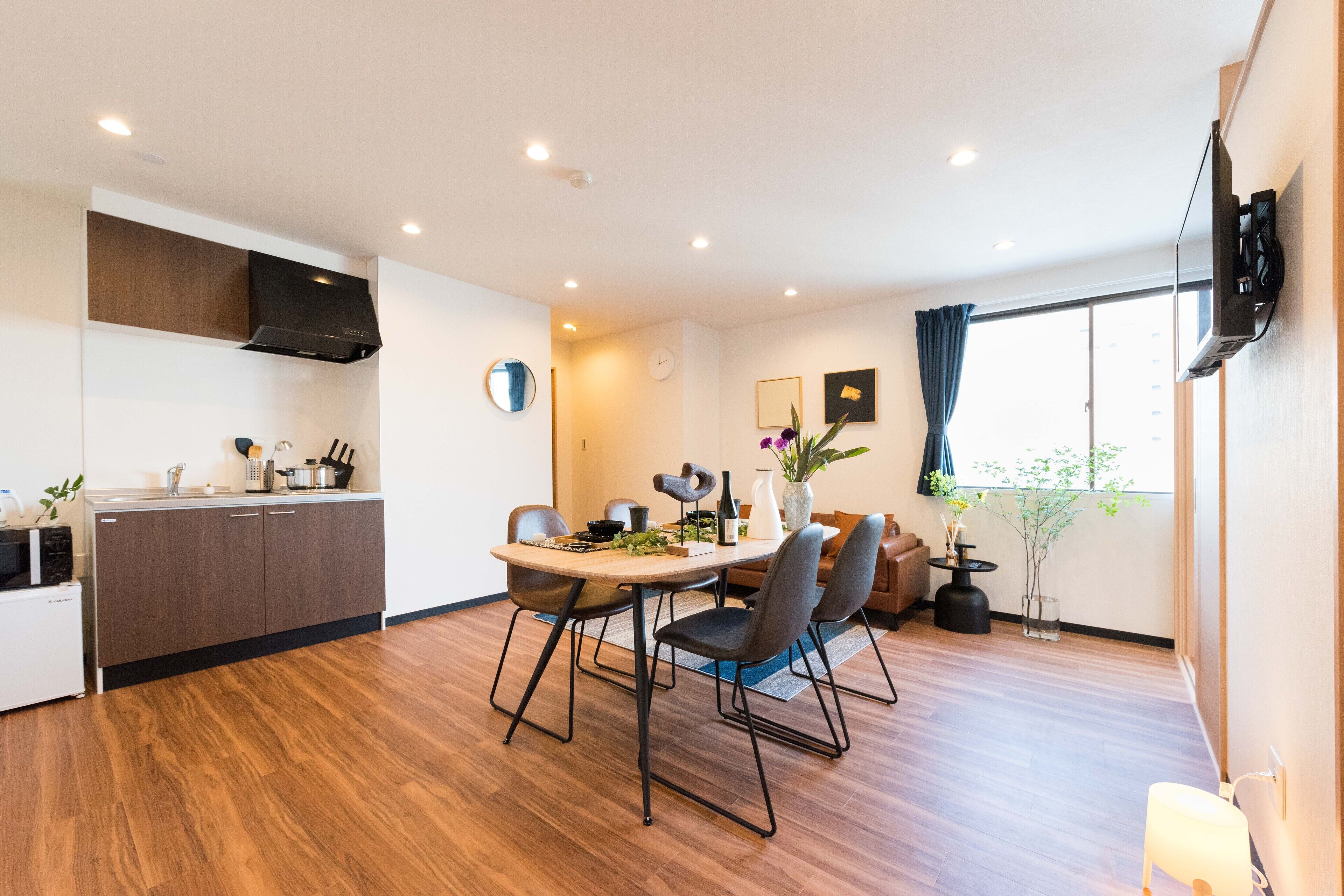 A modern kitchen with a dining area, wooden flooring, and a large window with curtains.
