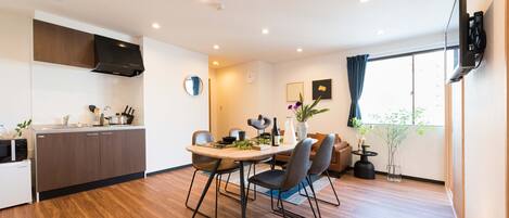 A modern kitchen with a dining area, wooden flooring, and a large window with curtains.