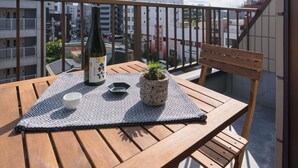 Une table en bois avec une bouteille, une tasse et une plante en pot, sur un balcon donnant sur la ville.