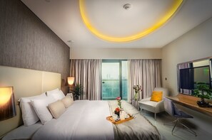 A modern hotel room with a large bed, a desk, a chair, and a view of the city.
