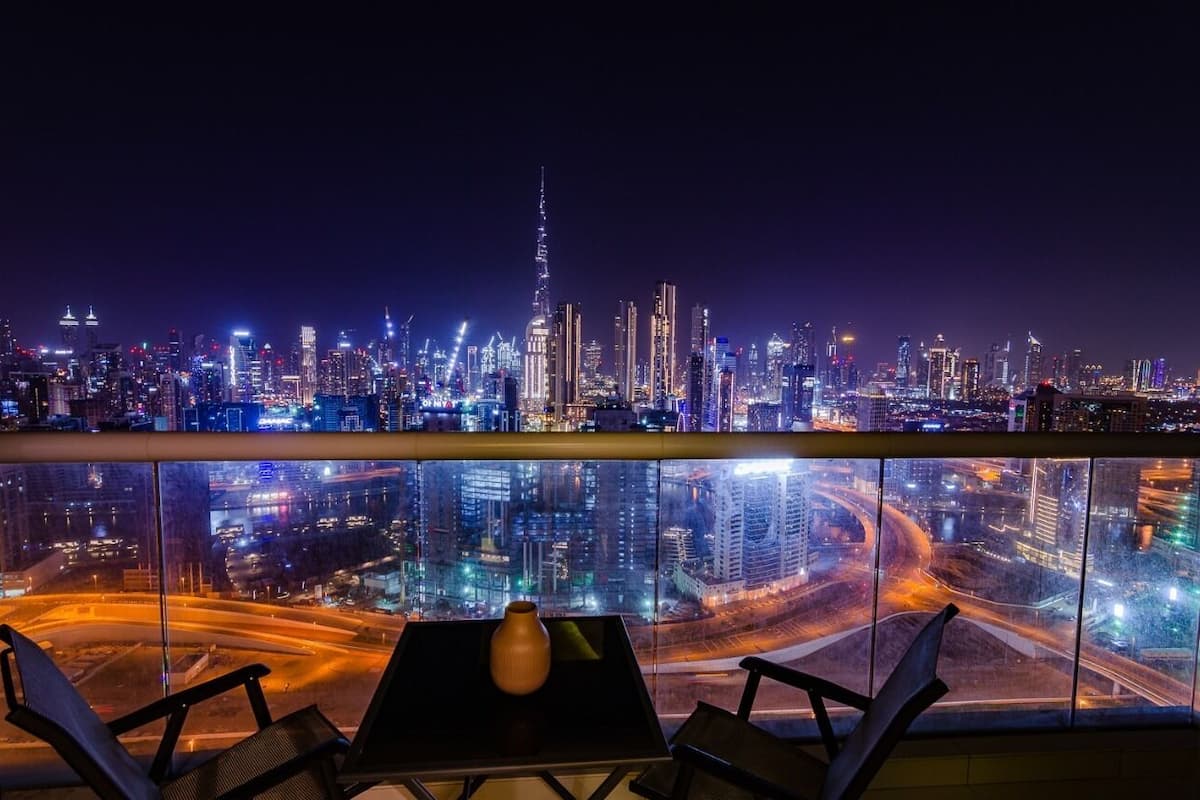 A night view of a city skyline from a high-rise hotel balcony with a table and chairs.