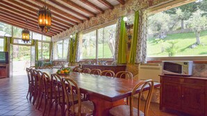 A dining area with a long wooden table, chairs, a television, and a stone wall with windows. - Nice home in Trabia with private swimming pool, can be inside or outside (Trabia)