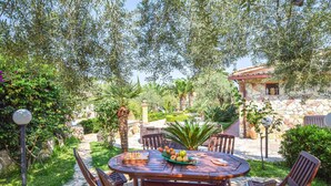 An outdoor dining area with a round wooden table and chairs, surrounded by lush greenery and a stone building in the background. - Nice home in Trabia with private swimming pool, can be inside or outside (Trabia)