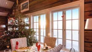 Une pièce chaleureuse, décorée d’un sapin de Noël, avec des fauteuils en osier et une table à manger dressée pour le repas.