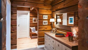 L’intérieur d’une cabane en rondins, avec un plancher en bois, une commode en bois dotée de tiroirs, une chaise, une lampe et des tableaux encadrés accrochés au mur.