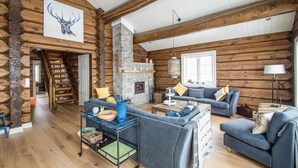 L’intérieur d’une cabane en rondins, avec une cheminée en pierre, des poutres en bois et un canapé bleu.