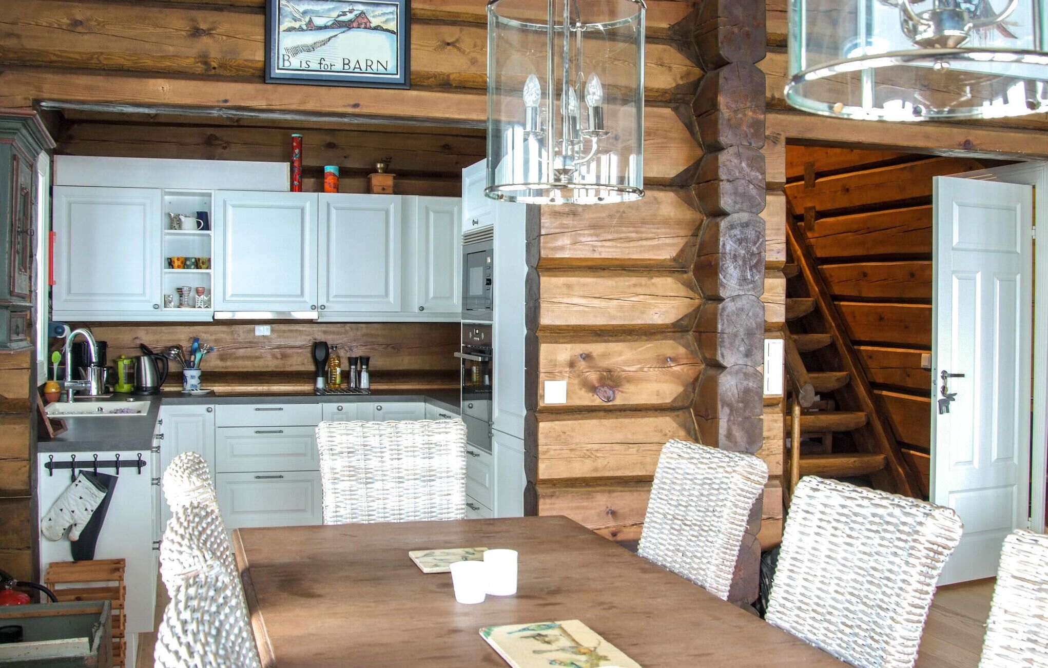 A rustic kitchen with white cabinets, a wooden dining table with wicker chairs, and a chandelier.