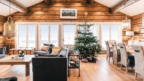 L’intérieur chaleureux d’un chalet en rondins, avec un plafond en bois, de grandes fenêtres, un sapin de Noël, des meubles en osier et un coin repas.