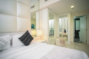 Une chambre moderne avec un grand lit, une table de chevet avec une lampe, un miroir et une vue sur la salle de bain.
