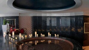 Un espace spa comprenant un jacuzzi circulaire, un coin salon agrémenté de bougies et un mur décoré de motifs.