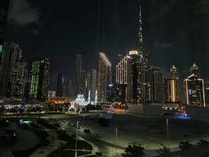 A nighttime cityscape with high-rise buildings, a prominent tower, and a well-lit mosque.
