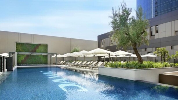 Una piscina con sillas de descanso y sombrillas, rodeada de vegetación y un edificio moderno.