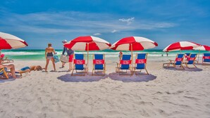 Een strand met rijen blauwe en rode strandstoelen en parasols, een zandstrand en de oceaan op de achtergrond.