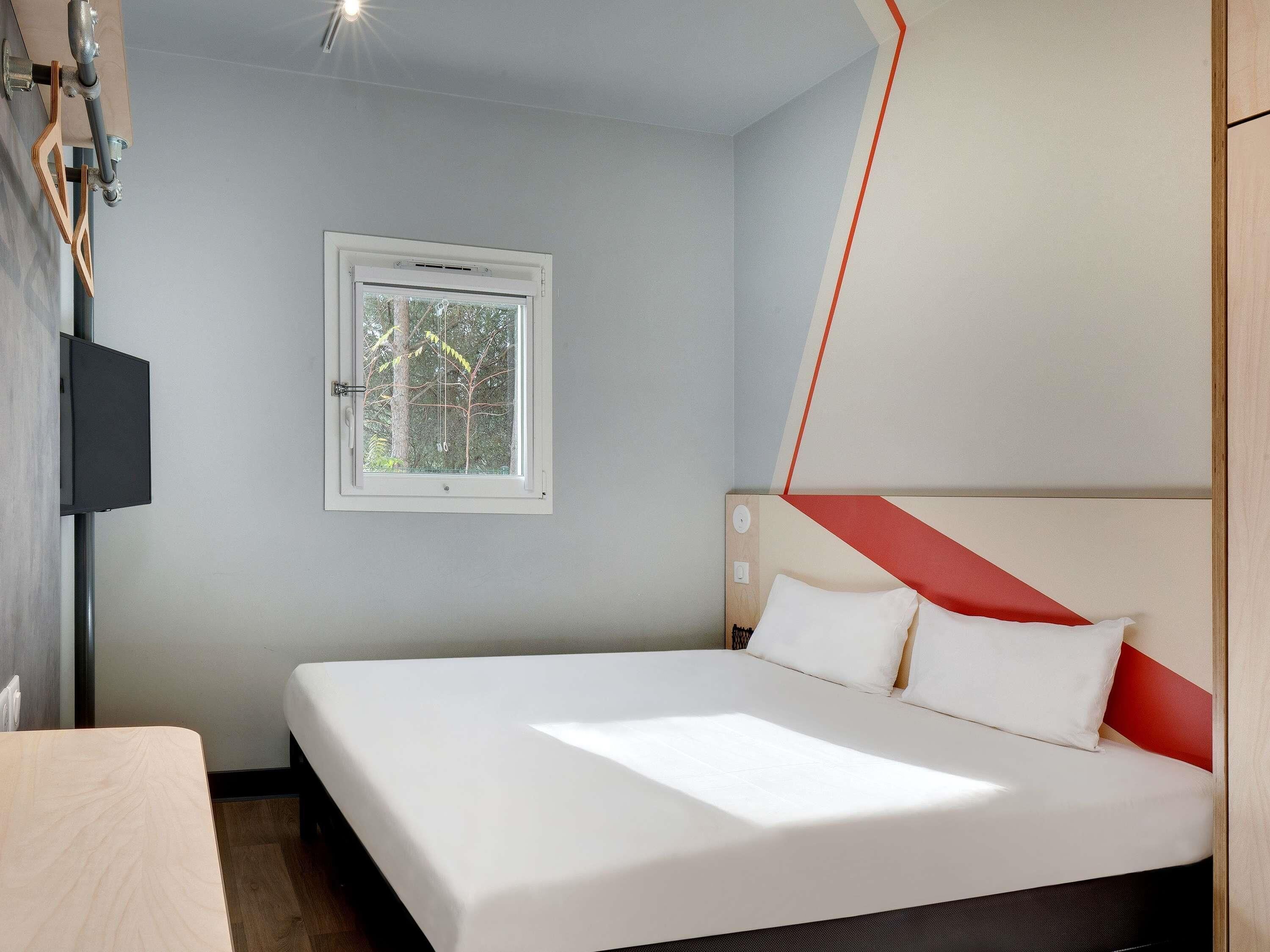 A bedroom with a bed, a window, and a wall-mounted TV.