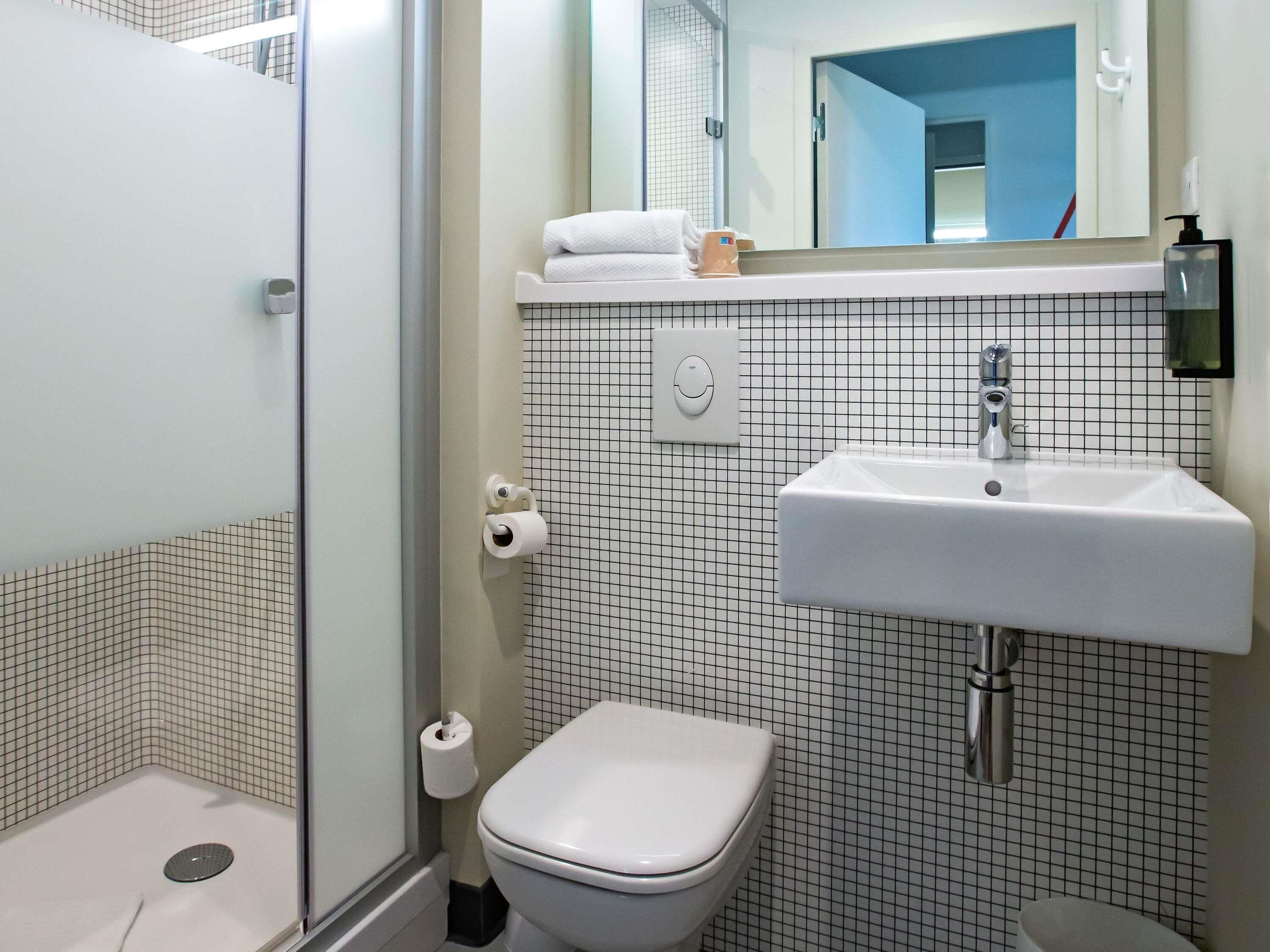 A bathroom with a white toilet, a sink, and a mirror. There is a towel rack above the sink and a toilet paper holder on the wall.