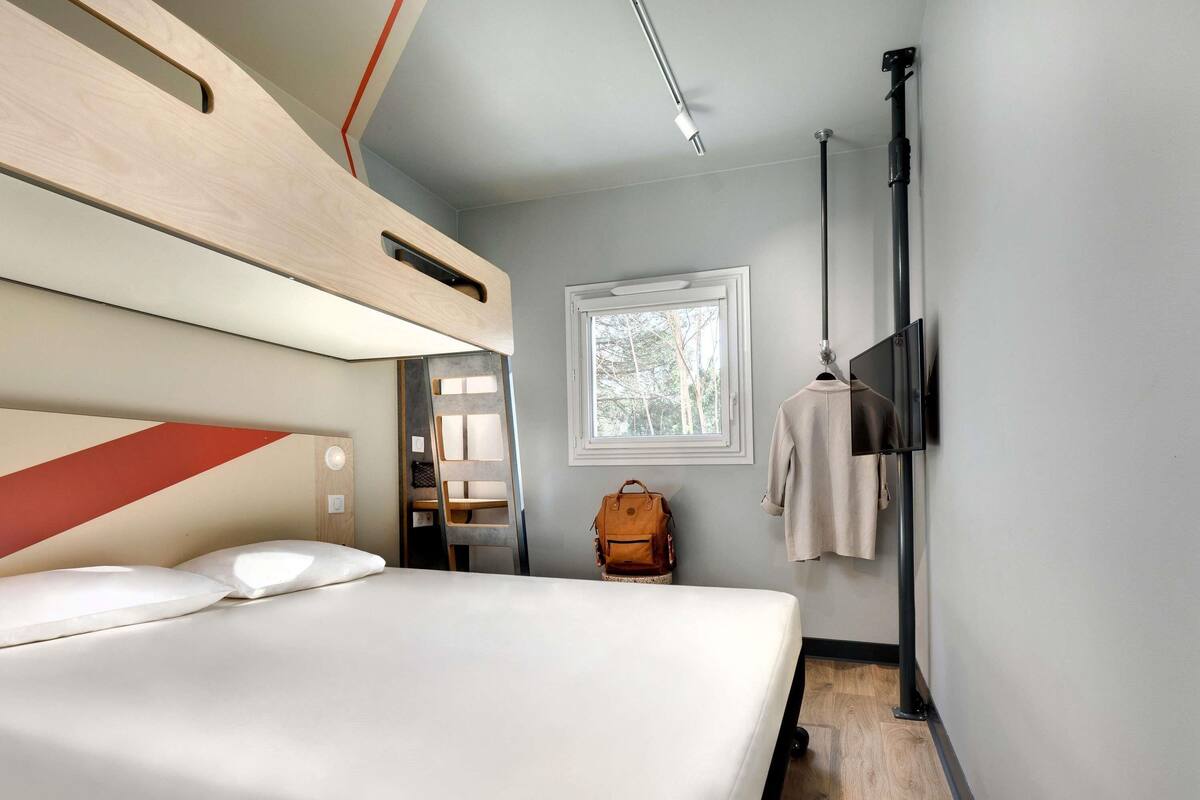 Une chambre avec un lit superposé, une table de chevet, une fenêtre donnant sur les arbres et un porte-manteau suspendu.