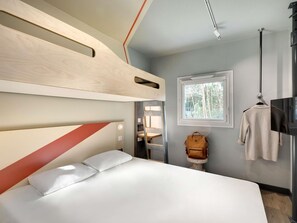 A modern bedroom with a bunk bed, a small table, a hanging TV, and a window with a view of trees.