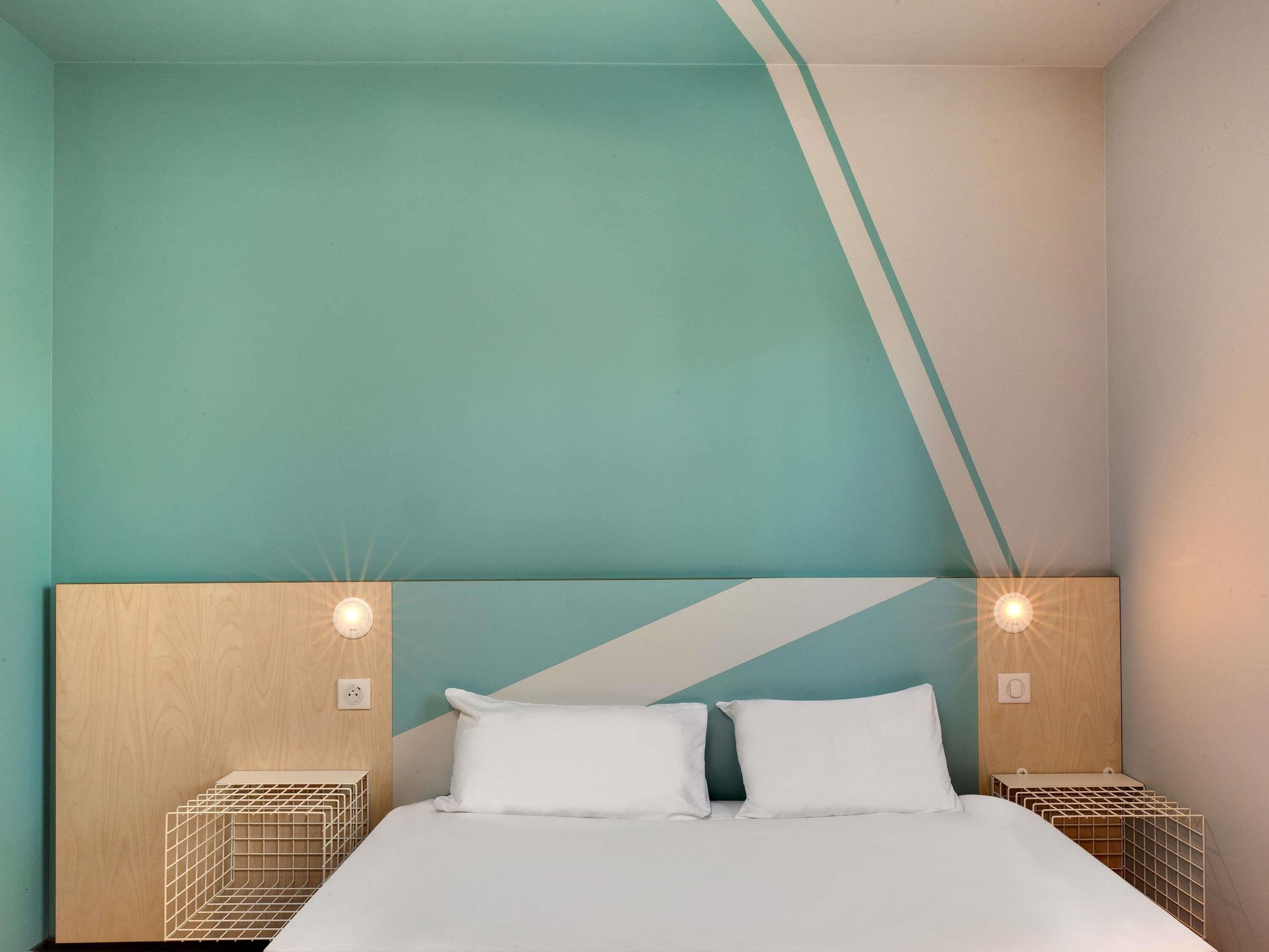 Une chambre moderne avec un grand lit, deux tables de chevet et un motif géométrique original sur le mur.