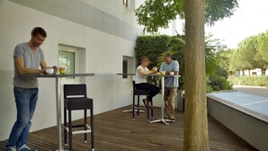 Un área de estar al aire libre con mesas y sillas, un árbol y vistas de la vegetación circundante.