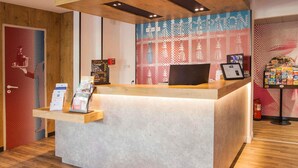 Un mostrador de recepción con una pantalla digital, una encimera de madera y una pared con diseño decorativo.