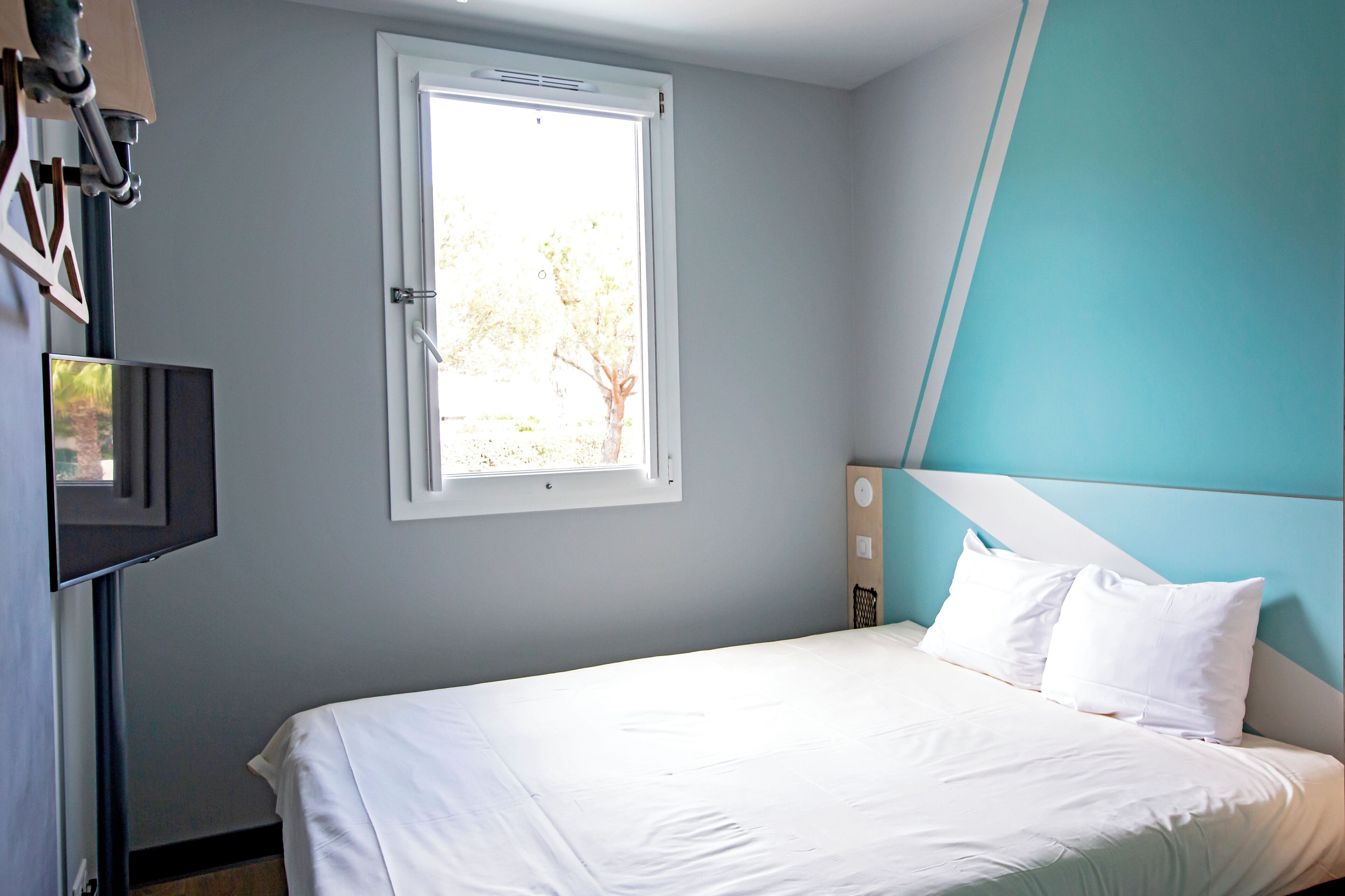 Une chambre à coucher avec un lit, une fenêtre et un téléviseur fixé au mur.