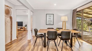 Un comedor moderno con una mesa de madera y sillas negras, un cartel enmarcado en la pared y un amplio ventanal con cortinas.