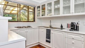 Cocina moderna con armarios blancos, horno empotrado y ventana con vistas a zonas verdes.