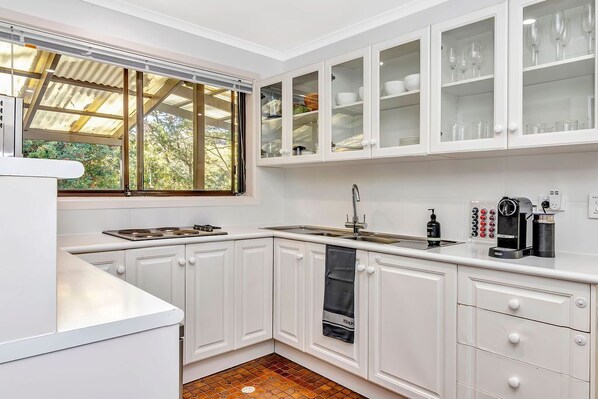 Cocina moderna con armarios blancos, horno empotrado y ventana con vistas a zonas verdes.