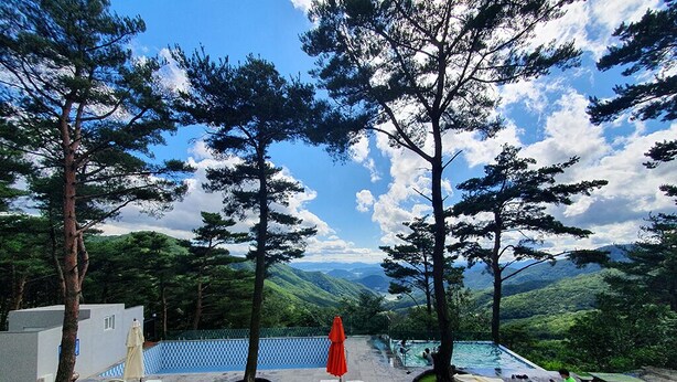 Un espace aménagé au bord de la piscine, avec des chaises longues, un parasol et une vue sur un paysage montagneux.
