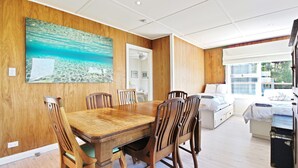 A dining area with a wooden table and chairs, a large painting of a beach scene, and a bedroom with a bed and a suitcase.