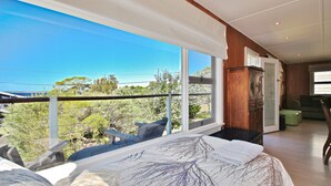 A bedroom with a large window overlooking a scenic landscape, a wooden cabinet, and a green ottoman.