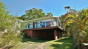 A two-story house with a balcony, surrounded by greenery and trees.