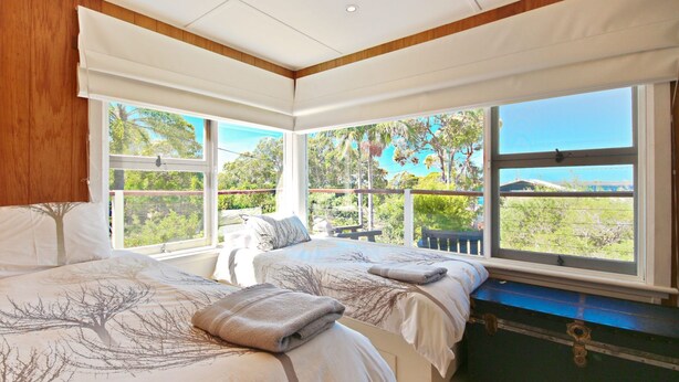 A bedroom with two beds, large windows, and a view of greenery.