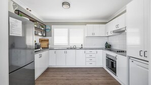 A modern kitchen with white cabinetry, a stainless steel refrigerator, a wooden countertop, and a built-in oven. - Akora House at Hyams Beach (Hyams Beach)