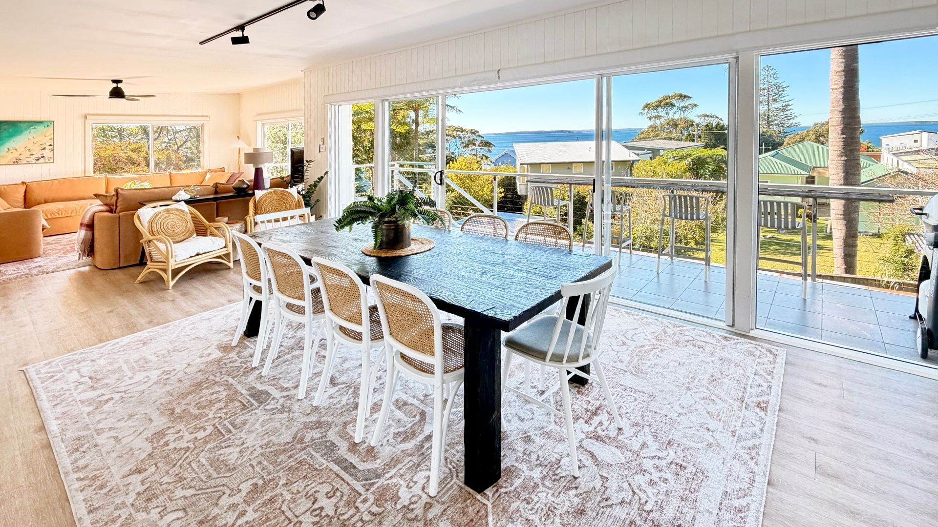 A spacious dining area with a large table and chairs, a view of the ocean, and a balcony with outdoor furniture.