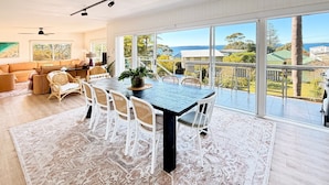 A spacious dining area with a large table and chairs, a view of the ocean, and a balcony with outdoor furniture. - Akora House at Hyams Beach (Hyams Beach)