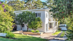 A modern two-story house with a covered patio, a small garden, and a staircase leading to a balcony. - Akora House at Hyams Beach (Hyams Beach)