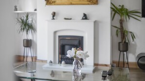 A living room with a glass coffee table, a vase with white flowers, a fireplace, and a television. - House - Sleeps 8 & On-site Parking (Aylesford)