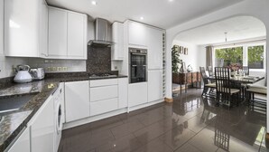 A modern kitchen with white cabinetry, granite countertops, and a dining area with a table and chairs. - House - Sleeps 8 & On-site Parking (Aylesford)