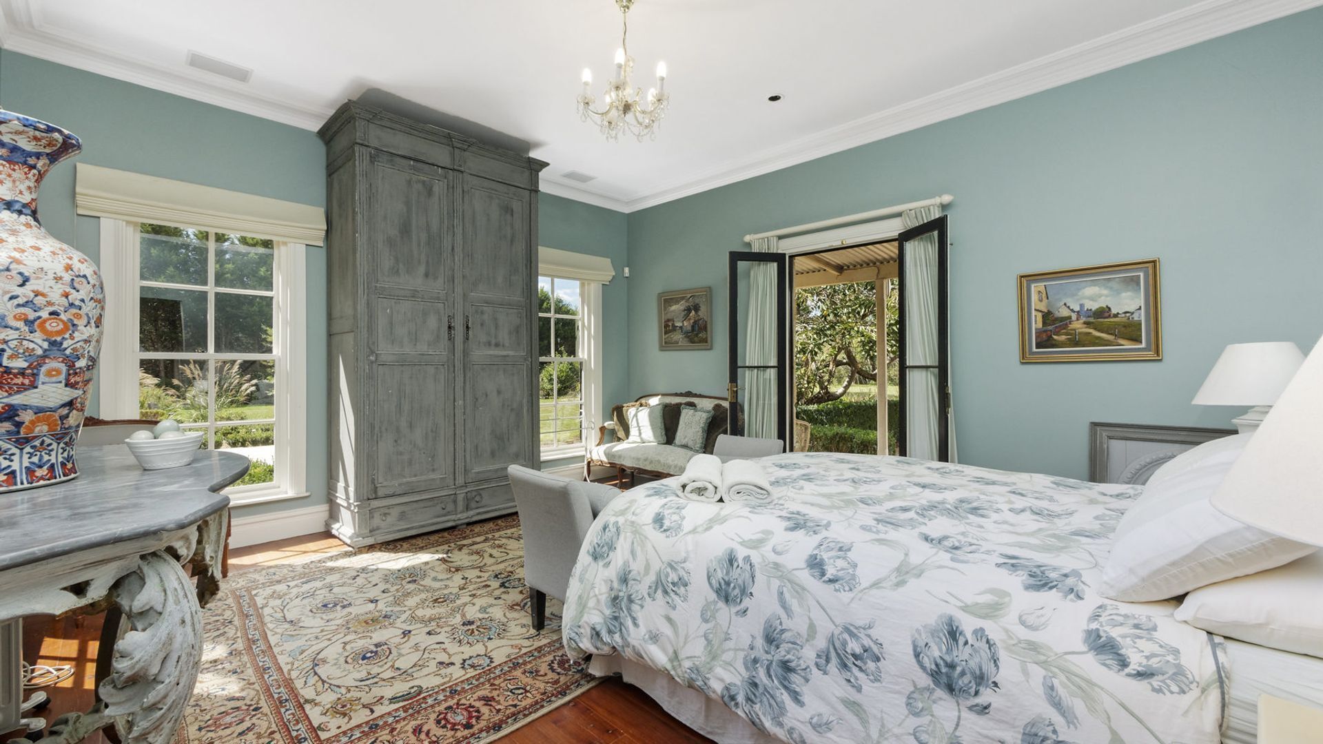 A bedroom with a large bed, a dresser, a chair, and a window with a view of greenery.