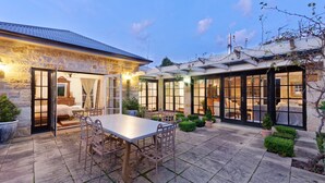 A stone building with a patio, a dining table, and chairs. - Aylmerton House + Cottage for 14, Southern Highlands (Mittagong)