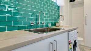 A kitchen with a stainless steel sink, a washing machine, and a green tiled backsplash. - Bay Breeze at Blenheim Beach, Vincentia (Vincentia)