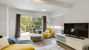 A modern living room with a flat-screen TV, a yellow armchair, a sofa, and a dining area with a table and chairs. - Bay Breeze at Blenheim Beach, Vincentia (Vincentia)