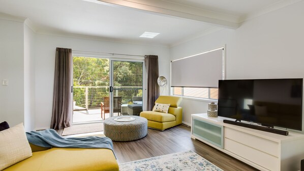 A modern living room with a flat-screen TV, a yellow armchair, a sofa, and a dining area with a table and chairs.