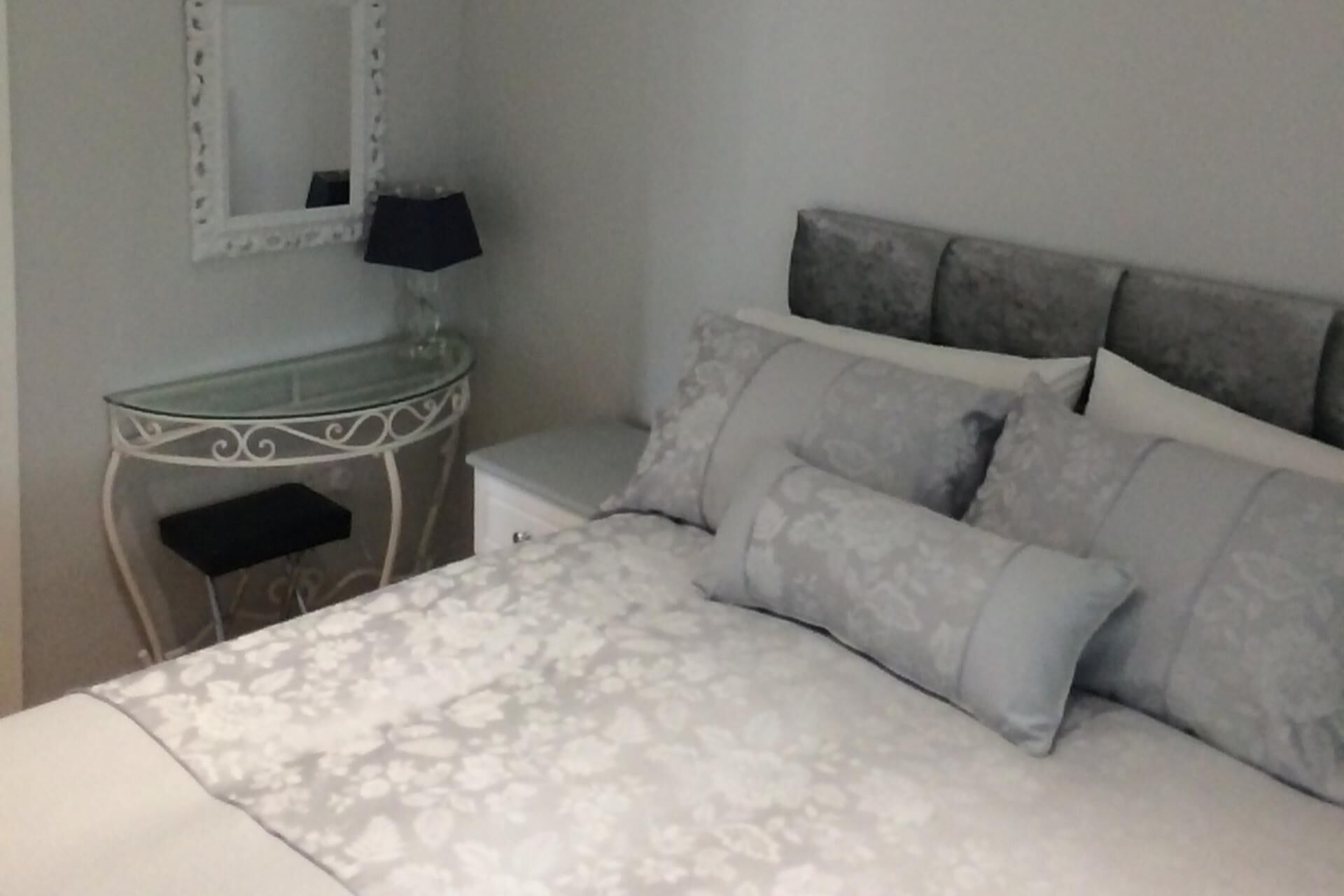 A bedroom with a bed, a bedside table, a mirror, and a lamp.